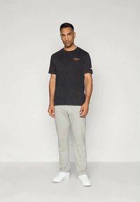 Sort T-shirt med korte ærmer og et lille logo, samt grå sweatpants. Skoene er hvide. Stoffet ser blødt ud og har en afslappet pasform.