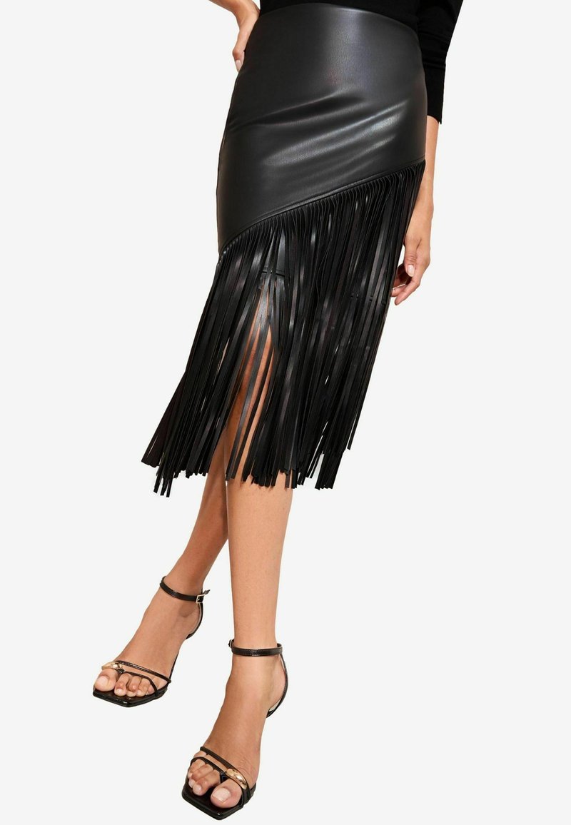 Zwarte faux leren rok met een asymmetrische zoom en lange franjes. Gecombineerd met zwarte sandalen met bandjes, die blote benen tonen.