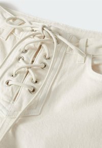 Shorts en coton crème avec un design à l'avant, œillets en métal et lacets, taille structurée et détails de couture diagonale.