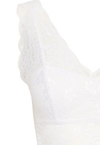 Bralette en dentelle blanche avec un décolleté à bord festonné et des bretelles, ornée d'un motif floral et d'une texture lisse et douce.