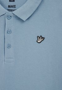 Gaiši zils polo krekls ar teksturētu audumu, trīs pogu aizdari un izšūtu melnbaltu putna logotipu krūšu daļā.