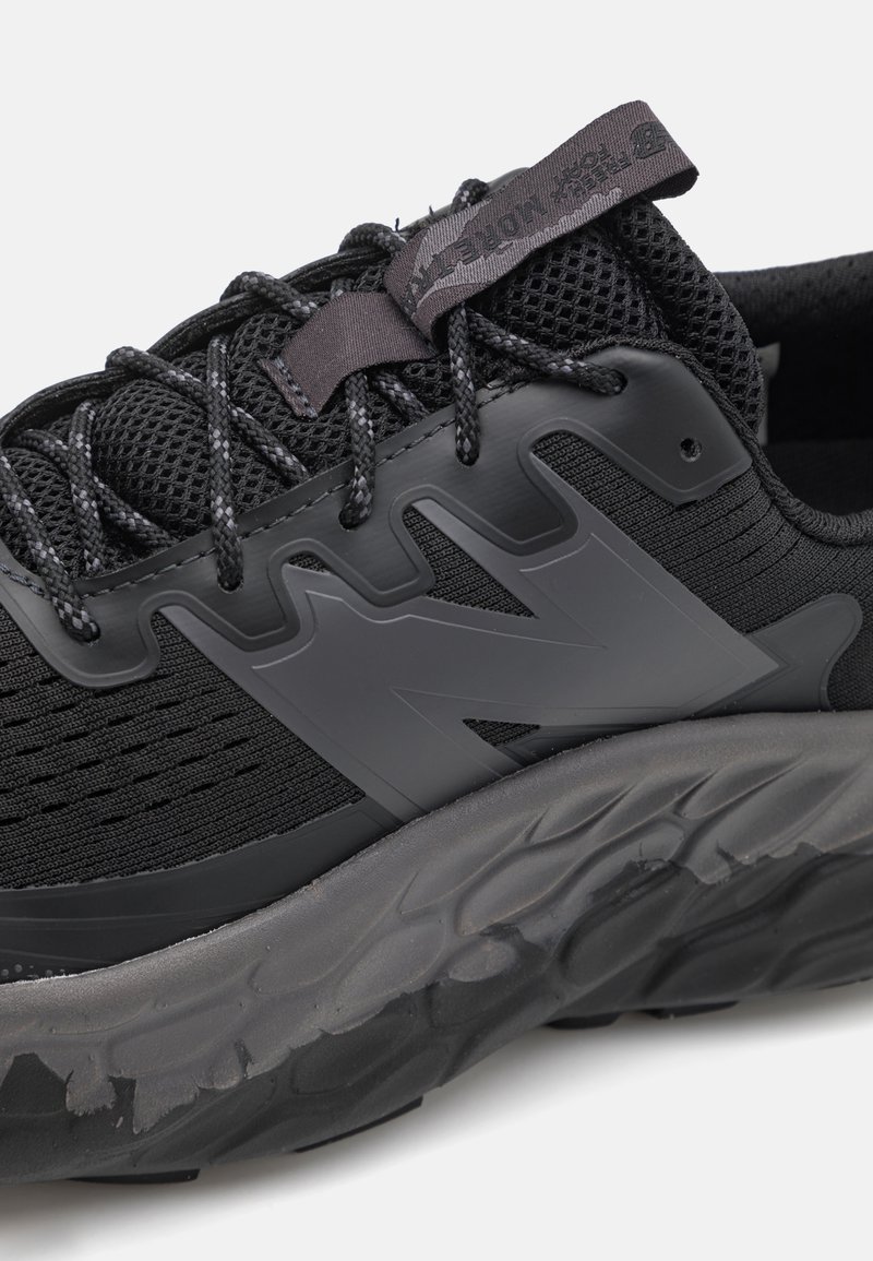 Zapato deportivo negro con parte superior de malla texturizada, logo "N" prominente y suela de goma gruesa con elementos de diseño en forma de onda.