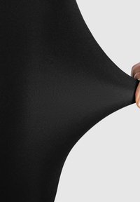 Mustaa joustavaa kangasta vedetään, jolloin näkyy sileä tekstuuri ja tiukka istuvuus. Materiaali näyttää ohuelta ja vartalonmyötäiseltä, ilman näkyviä kuvioita.