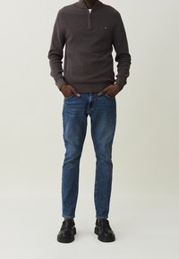 Tmavě šedý svetr se zipem, modré džíny a černé slip-on boty s tlustou podrážkou. Jednoduchý design, přiléhavý střih a texturovaná tkanina.