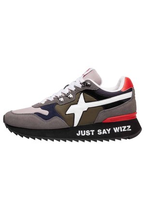 Niski sneaker z szarymi, czarnymi i oliwkowymi panelami, białym logo gwiazdy, białymi sznurowadłami, czerwonym akcentem na pięcie oraz napisem „JUST SAY WIZZ” na czarnej podeszwie.