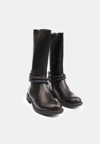 Botas de cuero negras hasta la rodilla con un diseño sencillo, que cuentan con un cierre de cremallera y cordones decorativos texturizados alrededor del eje superior.