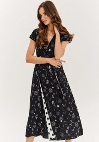 Černé zavinovací šaty se bílými grafickými potisky hvězd, srdcí a dalších symbolů. Krátké rukávy a knoflíkové detaily po straně.