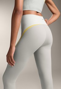 Világosszürke leggings sima textúrával, sárga díszcsíkkal és magas derékkal, párosítva egy illő cropped toppal.