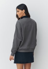 Harmaa collegepaita rentolla istuvuudella, resorireunuksin hihansuissa ja pääntiessä. Yhdistetty tummansiniseen farkkuhameeseen, jossa on hieman levenevä helma.