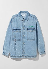 Ljusblå denimjacka med avslappnad passform, två framfickor och detaljer i vit färgsplatter. Har grön broderad text och tryck på sidan.