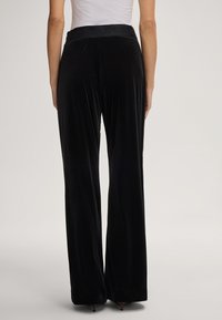 Zwarte fluwelen broek met een wijde pijpdesign, voorzien van een elastische tailleband met het merkteken, een zachte textuur en een vloerlange snit.