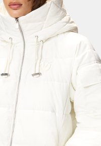 Giacca a piumino bianca con collo alto, chiusura con zip e dettagli con coulisse. Presenta un tessuto testurizzato e un logo in rilievo sul petto.