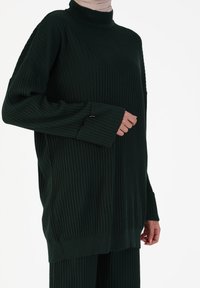 Maglione a collo alto a coste di colore verde scuro, con maniche lunghe e vestibilità comoda. Presenta un collo alto e una consistenza di maglia spessa.