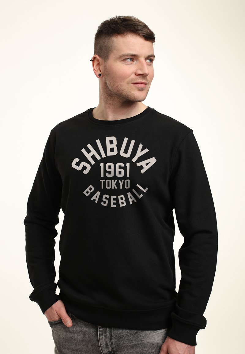 Felpa nera con colletto a giro e maniche lunghe. Testo grafico centrato "SHIBUYA 1961 TOKYO BASEBALL" in grigio chiaro. Tessuto morbido.