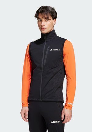 Zwarte Terrex vest met contrasterende oranje lange mouwen, voorzien van een hoge kraag, ritssluiting aan de voorkant en een geometrisch patroon op de onderkant van de voorkant.