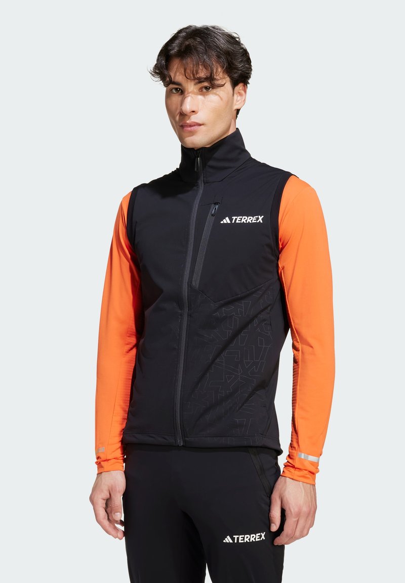 Schwarze Terrex-Weste mit kontrastierenden orangefarbenen langen Ärmeln, einem hohen Kragen, einem Reißverschluss vorne und einem geometrischen Muster am unteren Vorderteil.