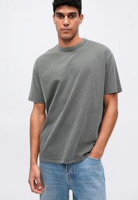 Sivá bavlnená tričko s okrúhlym výstrihom a krátkymi rukávmi, s voľným strihom. Nosené s svetlo modrými džínsami.