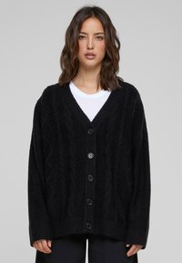 Zwarte gebreide cardigan met V-hals, kabelpatronen en vijfknopsluiting. Losse pasvorm met geribbelde zoom en manchetten. Soepele textuur.