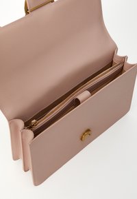 Lichtroze leren handtas met een afgeronde bovenkant, gouden hardware en een ritsvak. Het interieur heeft een gladde voering met een scheidingswand.