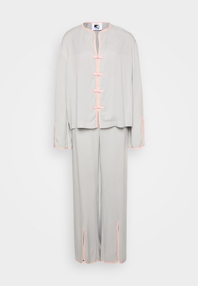 Costum format două piese, gri deschis, realizat dintr-un material moale. Are un guler mandarin, accente roz și butoane înnodate pe jachetă. Pantaloni largi cu fante.