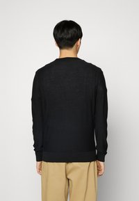 Maglione nero lavorato a maglia con scollo rotondo e polsini e orlo a costine. Tessuto leggero, texture morbida e vestibilità casual.