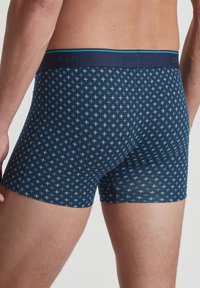 Navy boxer shorts feature a geometric pattern of light blue crosses, a soft fabric, and an elastic waistband with the brand name.
