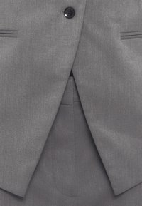 Γκρι κοστούμι από ύφασμα με ομαλή υφή, κλείσιμο με ένα μαύρο κουμπί, πέτο με εγκοπές και λοξές τσέπες. Ραμμένο σε εφαρμοστή γραμμή με καθαρές γραμμές.