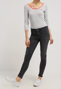T-shirt à manches longues rayé gris et blanc avec un col corail ; associé avec un jean slim noir et des baskets blanches.