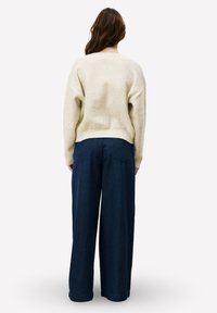 Pull en maille beige avec une coupe décontractée et des poignets côtelés, associé à un pantalon large en velours côtelé bleu foncé avec des poches arrière.