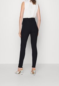 Svarta högmidjade byxor i ett glansigt tyg, med en figurnära passform, och kombinerade med ljusa klacksandaler.