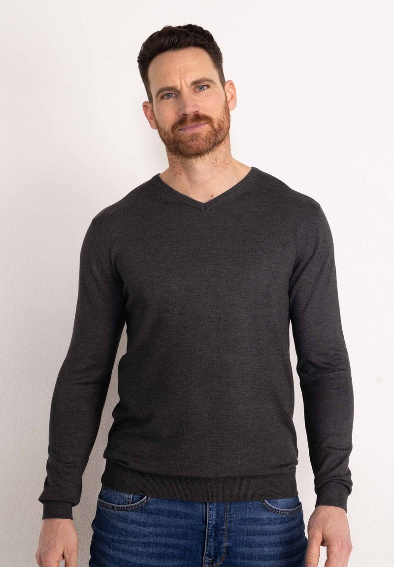 Maglione grigio scuro a V con maniche lunghe, realizzato in tessuto morbido, abbinato a jeans blu. Presenta un design aderente con polsini a costine.