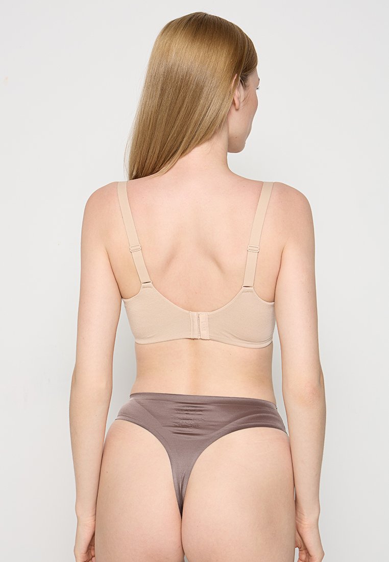 Beżowy biustonosz z regulowanymi ramiączkami i zapięciem na haczyk, w połączeniu z brązowym bezszwowym thongiem. Charakteryzuje się gładką teksturą i minimalistycznym designem.
