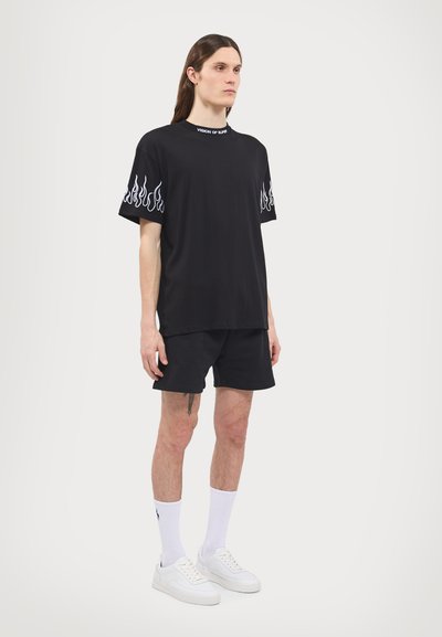 Must värvitooni lühikese varrukaga t-särk, millel on valged leekmustrid varrukatel, koos mustade lühikesed pükste ja valgete tossudega. Puuvillane kangas, mugav istuvus.