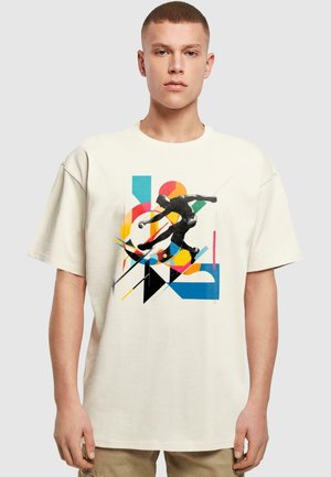 Cremefarvet oversized t-shirt med et grafisk design, der viser en sort skater og livlige geometriske figurer i orange, blå og gul.