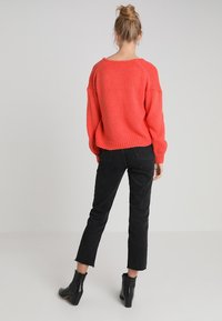 Maglione in maglia color corallo con vestibilità comoda e fondo costellato, abbinato a jeans neri cropped e stivaletti, visto da dietro.