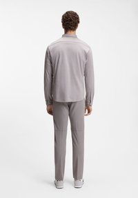 Γκρι πόλο πουκάμισο με μακριά μανίκια και διακριτή υφή, σε συνδυασμό με γκρι παντελόνι. Το σύνολο διαθέτει γιακά και μανσέτες με κουμπιά.