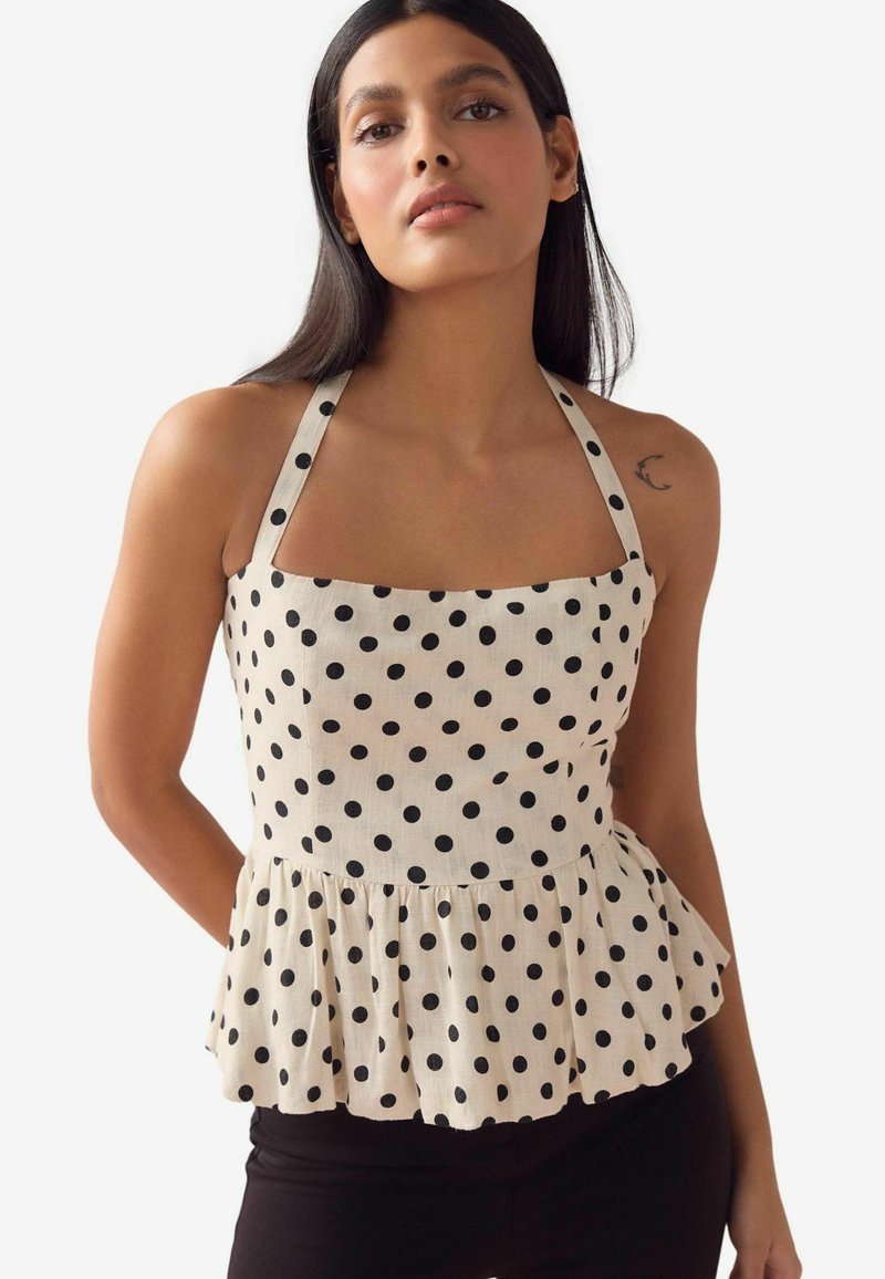 Peplum top v krémovej tkanine s čiernymi bodkami, štvorcovým výstrihom a nastaviteľnými ramienkami. Má zberaný lem pre tvar.