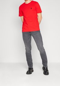 T-shirt rouge à manches courtes avec un col rond et un petit logo, associé à un jean slim gris et des bottines noires à semelles robustes.