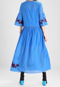Blauwe katoenen maxi-jurk met bellmouwen, voorzien van burgundy bloemen borduursels en een geplooide taille. Soepele, lichte textuur.