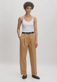 Beige, op maat gemaakte broeken met een hoge taille, scherpe plooien en zijzakken, gecombineerd met een witte tanktop en een zwarte riem. Zwarte platte schoenen.