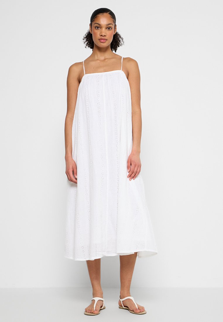 Vestido maxi blanco sin mangas con patrón de ojales, tejido fluido y silueta recta. Luce con sandalias planas, sobre un fondo liso.