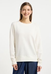 Pullover bianco leggero realizzato in tessuto testurizzato, con scollatura rotonda e maniche lunghe, abbinato a pantaloni in denim scuro.