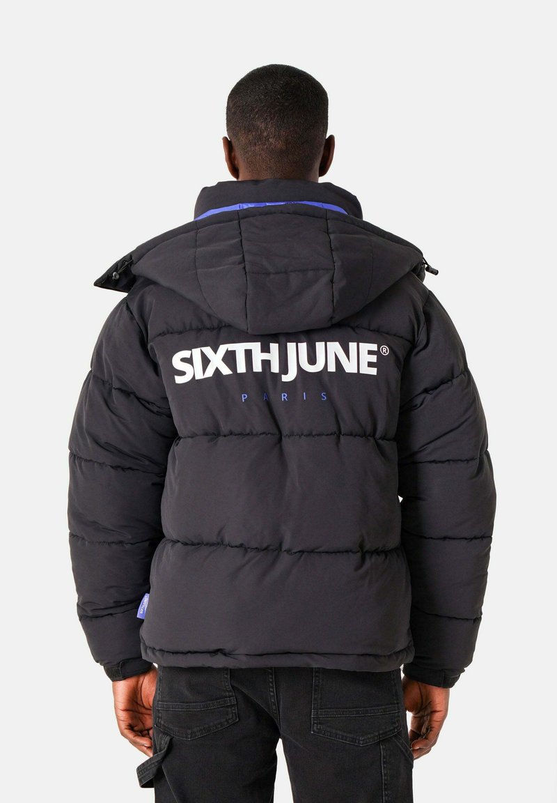Zwarte pufferjack met capuchon, blauwe accenten en grote witte "SIXTHJUNE" branding op de achterkant. Gestructureerd gewatteerd ontwerp voor isolatie.