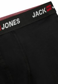 Zwarte stretch boxershorts hebben een brede elastische tailleband in zwart met rode accenten en witte "JACK JONES" branding. Naadloos ontwerp.