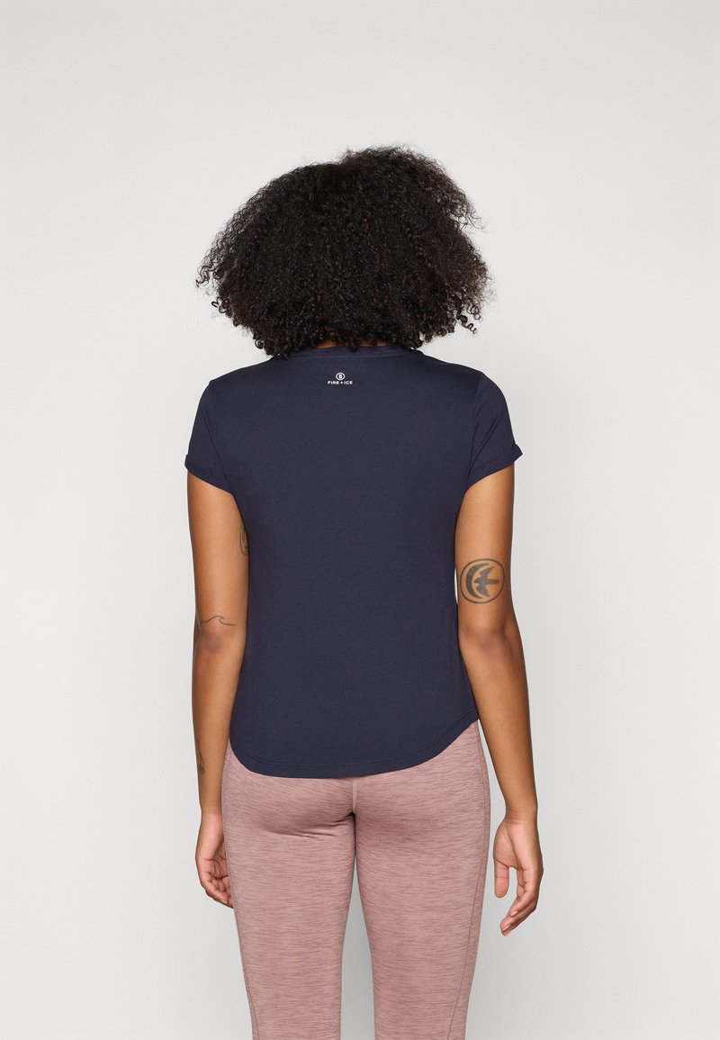 Dunkelblaues T-Shirt mit kurzen Ärmeln und abgerundetem Saum, das auf der oberen Rückseite ein kleines Logo trägt, kombiniert mit hellrosa enganliegenden Leggings.