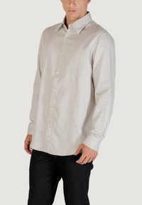 Camicia a maniche lunghe grigio chiaro con un motivo a righe, colletto button-down e piccoli bottoni. Il tessuto appare liscio e leggermente strutturato.
