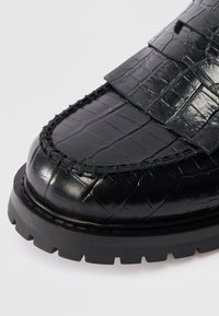 Schwarze Lederloafer mit Krokodillederstruktur, Mokassin-Nähten, dicke profilierte Sohle und breitem Riemen über dem oberen Teil.