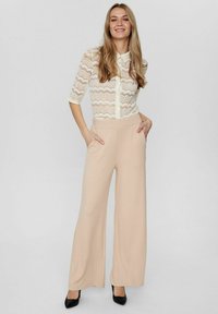 Spetsblus med knappar och trekvartsärmar, tillsammans med hög midja och vida beige byxor. Svarta klackskor fulländar outfiten.