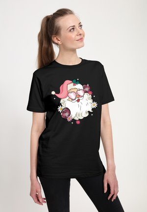 Smilende person iført sort skjorte med tegneserie-julemand i pink hat og hjerteformede solbriller, omgivet af blomster og diskokugler, kigger op.