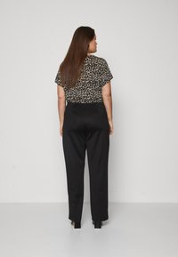 Zwarte wijde broek gedragen met een kortmouwige top met luipaardprint, met een relaxte pasvorm en een gladde textuur. Model gezien van achteren.